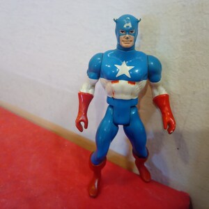 Pode incluir: Uma figura de a&ccedil;&atilde;o vintage do Capit&atilde;o Am&eacute;rica, vestindo um traje azul e vermelho com uma estrela branca no peito. A figura tem um capacete vermelho e azul com uma estrela branca na frente.