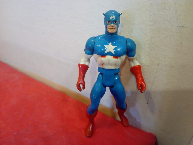 Pode incluir: Uma figura de a&ccedil;&atilde;o vintage do Capit&atilde;o Am&eacute;rica, vestindo um traje azul e vermelho com uma estrela branca no peito. A figura tem um capacete vermelho e azul com uma estrela branca na frente.