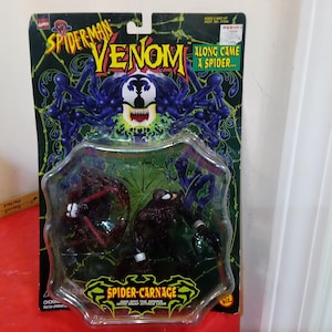 Może przedstawiać: Zestaw figurek Spider-Man Venom i Spider-Carnage w oryginalnym opakowaniu. Opakowanie jest czarno-zielone z nadrukami "Spider-Man Venom" i "Along Came a Spider...". Figurki znajdują się w przezroczystym plastikowym blistrze.