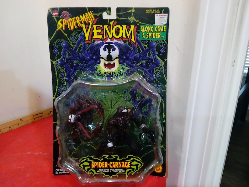 Może przedstawiać: Zestaw figurek Spider-Man Venom i Spider-Carnage w oryginalnym opakowaniu. Opakowanie jest czarno-zielone z nadrukami "Spider-Man Venom" i "Along Came a Spider...". Figurki znajdują się w przezroczystym plastikowym blistrze.