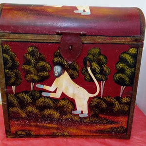 May include: A vintage wooden chest painted with a red background and a white monkey with a blue face and blue shoes. The monkey is surrounded by green trees and yellow foliage. The chest has a metal latch and hinges.