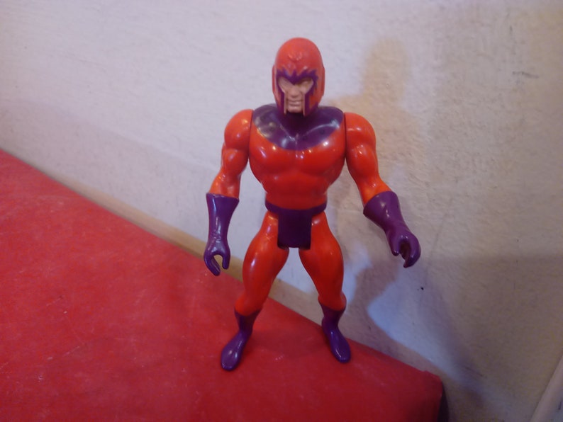 Pode incluir: Uma figura de a&ccedil;&atilde;o vermelha e roxa de um super-her&oacute;i com capacete. A figura tem uma constru&ccedil;&atilde;o muscular e est&aacute; de p&eacute; com os bra&ccedil;os ao lado do corpo.