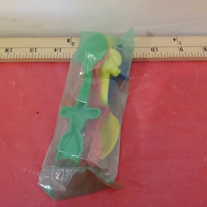 May include: A package of four plastic spoons in green, yellow, red, and blue. The spoons are shaped like different animals.