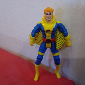 Pode incluir: Uma figura de a&ccedil;&atilde;o azul e amarela com uma capa amarela e um cinto vermelho. A figura tem uma cabe&ccedil;a amarela com cabelo laranja e uma express&atilde;o s&eacute;ria.