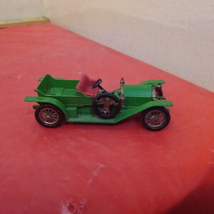 May include: A green toy car with a red seat and black wheels. The car is a vintage model with a long hood and a spare tire on the back.