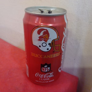 Op de afbeelding: Een rode aluminium blikje Coca-Cola Classic met het logo van de Tampa Bay Buccaneers. Het blikje heeft het NFL-logo en de tekst "1992 Collector Series".