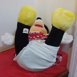 Puede incluir: Un juguete de peluche de Minnie Mouse con un vestido de lunares rojos y blancos y ropa interior blanca. El juguete tiene manos y pies amarillos y ojos negros. El juguete est&aacute; acostado de espaldas con las piernas en el aire. El juguete tiene una etiqueta "Disney" en su pierna.