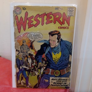 Może przedstawiać: Okładka komiksu Western Comics z epoki, przedstawiająca kowboja z bronią, w żółtej koszuli i niebieskiej kurtce. Tekst na okładce brzmi "Western Comics" i "Give up your gun, Savage! We're takin' over the herd!" Komiks przedstawia Matta Savage'a, szefa szlaku w "Revolt in Painted Canyon!"