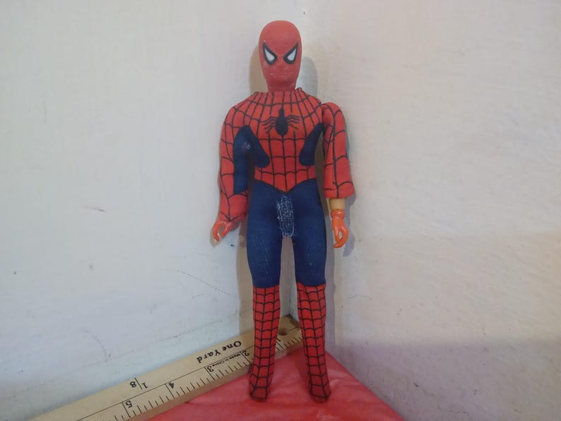 May include: A red and blue Spider-Man action figure with a black spider logo on the chest. The figure has a red mask with white eyes and is posed with arms outstretched.