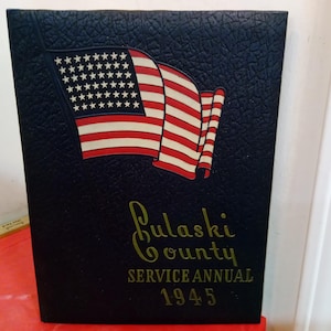 May include: A navy blue book cover with an American flag graphic. The flag is red, white, and blue. Gold text reads "Pulaski County Service Annual 1945". The cover has a textured appearance.