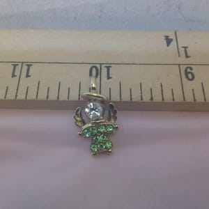 May include: A small gold angel charm with green and clear rhinestones. The charm is about 1 inch tall and is perfect for adding a touch of sparkle to any jewelry project.