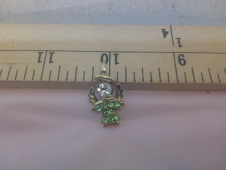 May include: A small gold angel charm with green and clear rhinestones. The charm is about 1 inch tall and is perfect for adding a touch of sparkle to any jewelry project.
