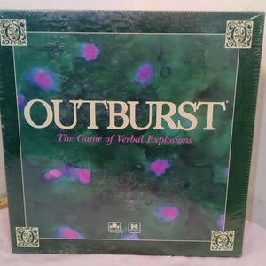 May include: A green board game box with the title "Outburst: The Game of Verbal Explosions" in white letters. The box has a green background with pink and purple watercolor splatters.