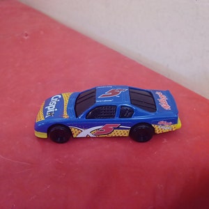 May include: A blue toy race car with a yellow and red "Cripix" logo and the number "5" on the side. The car has a black windshield and black wheels.
