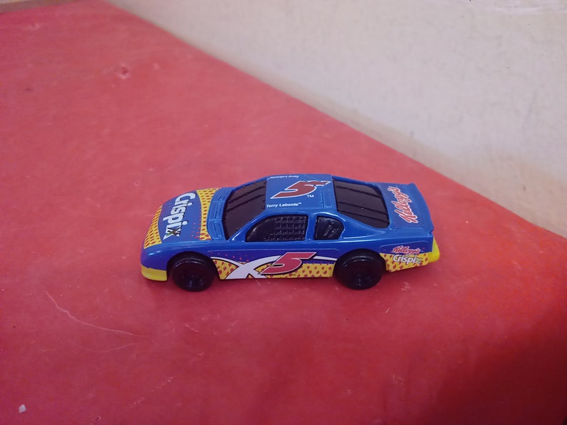 May include: A blue toy race car with a yellow and red "Cripix" logo and the number "5" on the side. The car has a black windshield and black wheels.