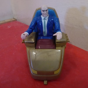 Pode incluir: Uma figura de a&ccedil;&atilde;o de pl&aacute;stico azul e dourado do Professor X dos X-Men, sentado em uma cadeira dourada com um assento azul. A cadeira tem rodas e um design dourado e preto.