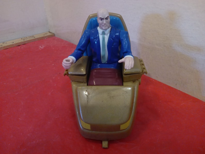 Pode incluir: Uma figura de a&ccedil;&atilde;o de pl&aacute;stico azul e dourado do Professor X dos X-Men, sentado em uma cadeira dourada com um assento azul. A cadeira tem rodas e um design dourado e preto.