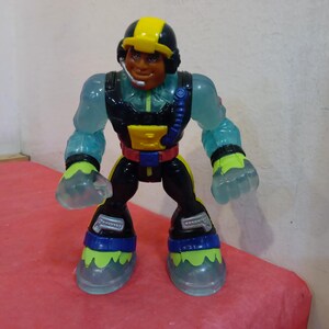 May include: A translucent blue action figure with a yellow helmet, black and red suit, and a black microphone. The figure has a black and blue belt and yellow and green boots.