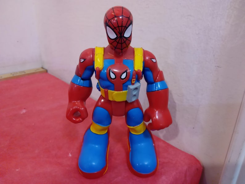 May include: A red and blue action figure of Spider-Man with a web shooter on his arm. The figure has a red and blue suit with a yellow belt and a black spider logo on the chest.