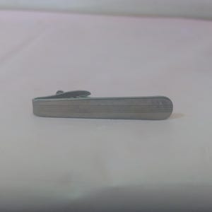 May include: A silver tie clip with a textured surface.