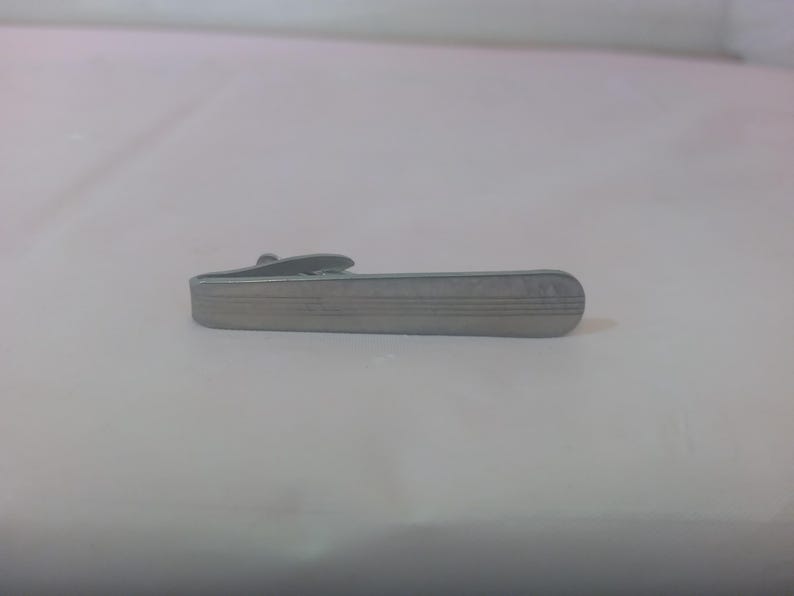 May include: A silver tie clip with a textured surface.