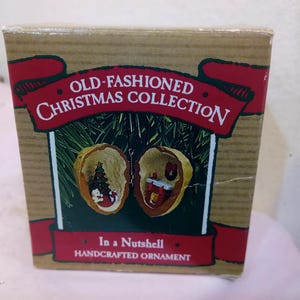 May include: A boxed, handcrafted Christmas ornament from the "Old-Fashioned Christmas Collection." The ornament is a walnut shell, split open to reveal miniature scenes. One side features a Christmas tree and snowman, the other a fireplace scene.