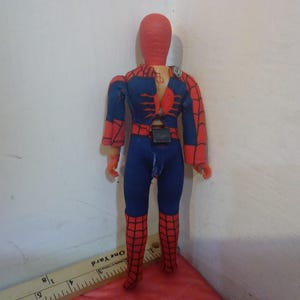 May include: A red and blue action figure of Spider-Man with a web design on the chest and legs. The figure has a red head and a black belt.