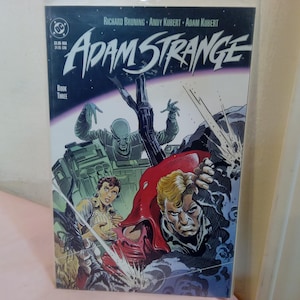 May include: A comic book cover featuring Adam Strange, a science fiction superhero. The cover is illustrated with Adam Strange in a red and black suit, fighting a group of aliens. The cover text reads "Adam Strange" in a bold, white font.