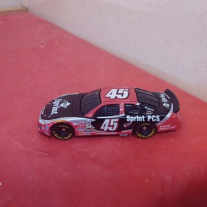May include: A red, black, and silver toy race car with the number 45 on the side. The car is a Sprint PCS sponsored car.