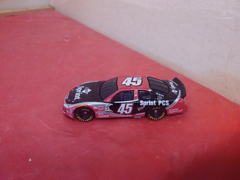 May include: A red, black, and silver toy race car with the number 45 on the side. The car is a Sprint PCS sponsored car.