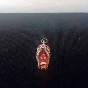May include: A silver charm in the shape of a red and green flip-flop with a star on top.