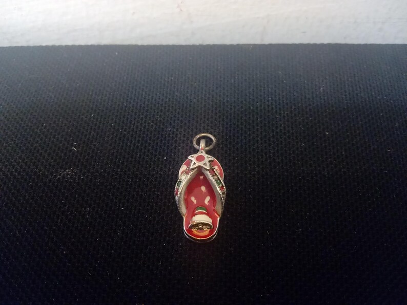 May include: A silver charm in the shape of a red and green flip-flop with a star on top.