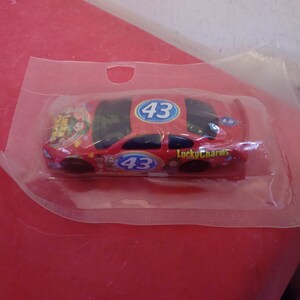 May include: A red toy race car with the number 43 on the side and the words "Lucky Charms" printed on the car. The car is in a clear plastic bag.