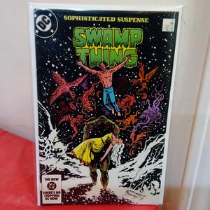Könnte beinhalten: Ein Swamp Thing Comic mit schwarzem Cover, das eine Figur in blauen Jeans und eine in Gelb gekleidete Person in den Armen eines Sumpfmonsters zeigt. Der Text lautet Sophisticated Suspense, Swamp Thing und The New DC There's No Stopping Us Now.