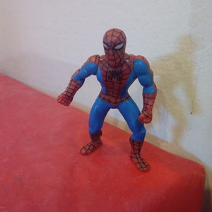 Pode incluir: Uma figura de a&ccedil;&atilde;o de pl&aacute;stico vermelha e azul do Homem-Aranha. A figura tem um s&iacute;mbolo de aranha preto no peito e est&aacute; em posi&ccedil;&atilde;o de p&eacute; com os bra&ccedil;os estendidos.