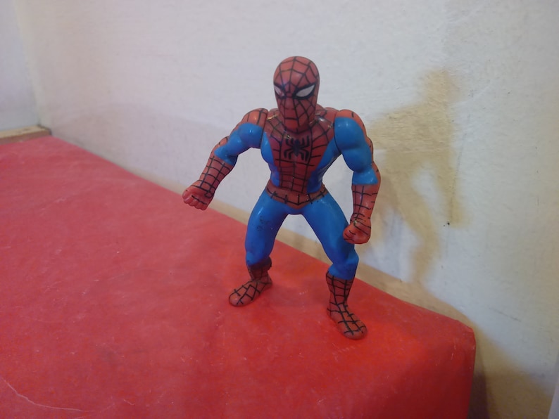 Pode incluir: Uma figura de a&ccedil;&atilde;o de pl&aacute;stico vermelha e azul do Homem-Aranha. A figura tem um s&iacute;mbolo de aranha preto no peito e est&aacute; em posi&ccedil;&atilde;o de p&eacute; com os bra&ccedil;os estendidos.