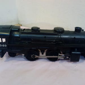 May include: Black toy train with the number 8040 on the side. The train has multiple wheels and a detailed design, including a smokestack and a front cowcatcher. The toy train is a classic model.