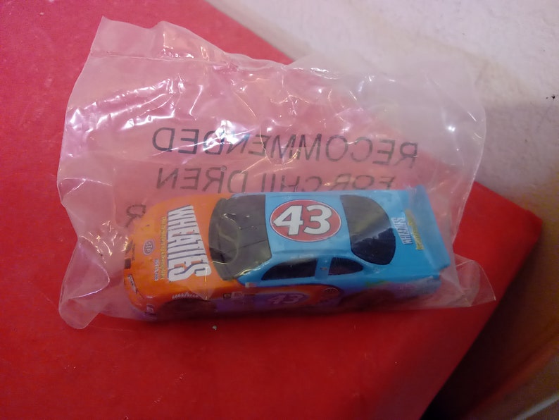 May include: A blue and orange toy race car with the number 43 on the side and the word "Wheaties" on the side. The car is in a clear plastic bag with the words "For Children Recommended" printed on the bag.