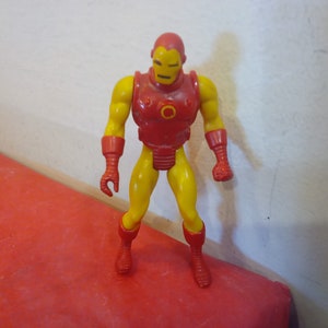 Pode incluir: Uma figura de a&ccedil;&atilde;o vintage do Homem de Ferro, um super-her&oacute;i com um traje vermelho e amarelo, em p&eacute; sobre uma superf&iacute;cie vermelha.