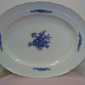 May include: A white oval serving platter with a blue floral design. The platter has a raised rim and a scalloped edge.