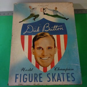 Może przedstawiać: Winietkowe pudełko na łyżwy figurowe mistrza świata Dicka Buttona. Pudełko zawiera czerwoną, białą i niebieską tarczę z portretem Dicka Buttona i tekstem "Dick Button World Champion Figure Skates".
