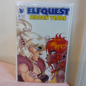 Puede incluir: Portada de cómic de Elfquest: Hidden Years #4. La obra de arte presenta dos personajes elfos con orejas puntiagudas, uno con cabello rubio y el otro con cabello rojo, uno frente al otro. El título está en azul y amarillo.
