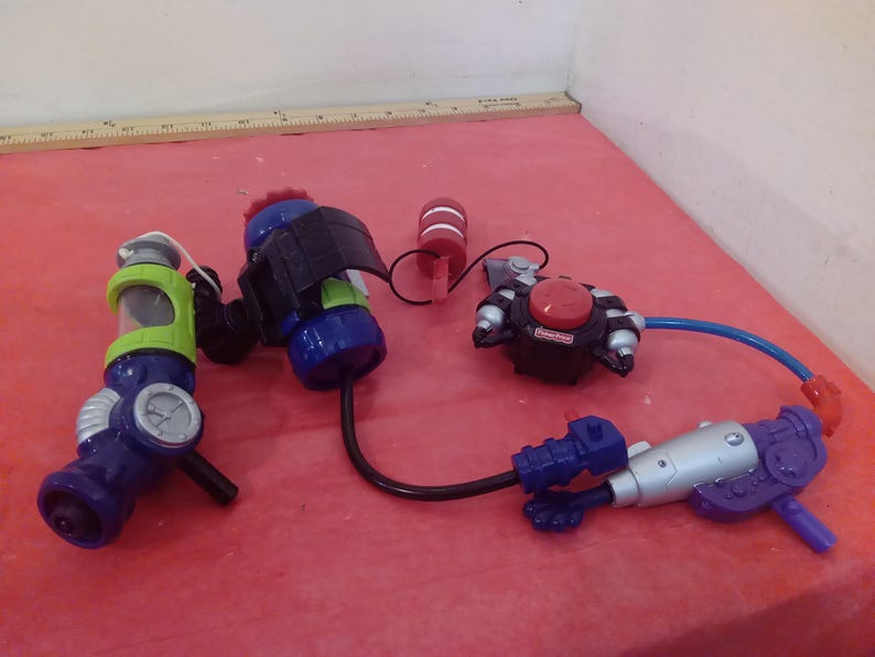 May include: A set of four toy water guns, including a green and blue gun with a clear tank, a blue and black gun with a black strap, a red and black gun with a red button, and a silver and purple gun with a blue handle.