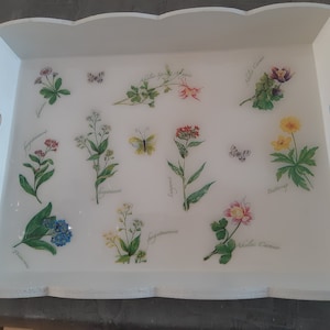 Peut inclure: Plateau de service en bois blanc avec un motif floral décoratif. Le plateau présente diverses fleurs et papillons, notamment des myosotis, des alchémilles et des carottes sauvages. Le plateau est parfait pour servir des en-cas, des boissons ou d'autres articles.