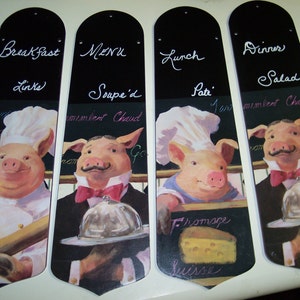 May include: Four black chalkboard fan blades with pig chef illustrations. Each blade features a different menu category: Breakfast, Menu, Lunch, and Dinner. The text on the blades reads: "Breakfast Links", "Menu Soupe'd", "Lunch Pate", and "Dinner Salad".