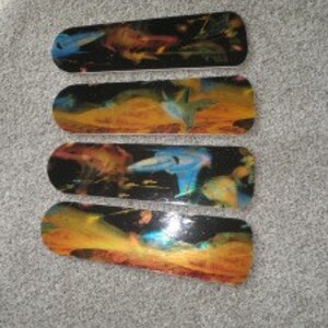 May include: Four skateboard decks with a colorful abstract design. The decks feature a black base with vibrant splashes of orange, yellow, blue, and green. Each deck has a unique pattern, creating a dynamic and artistic look. The decks are arranged on a gray surface.