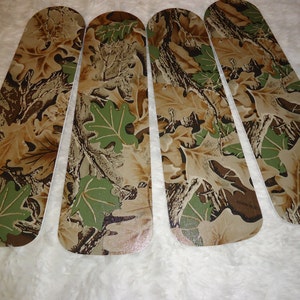 May include: Four camouflage-patterned ceiling fan blades with a brown, green, and tan color scheme. The blades have a leaf design.