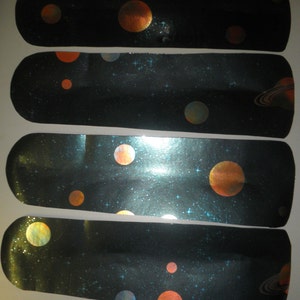 May include: Four black and blue fan blades with a space theme. The blades have a glittery finish and feature orange and yellow planets, stars, and a ringed planet.