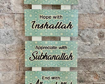 Op de afbeelding: Een set van vier houten borden met een turquoise en wit geometrisch patroon. Elk bord heeft een andere islamitische zin in zwarte letters: "Begin met Bismillah", "Hoop met Inshallah", "Waardeer met Subhanallah" en "Einde met Alhamdulillah".