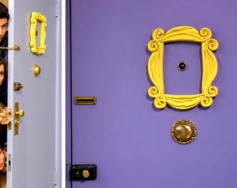 May include: A purple door featuring a prominent yellow decorative frame surrounding a central peephole. Below the frame is a round brass knob. A smaller yellow frame is visible on the adjacent door edge, along with a brass handle, lock, and chain.